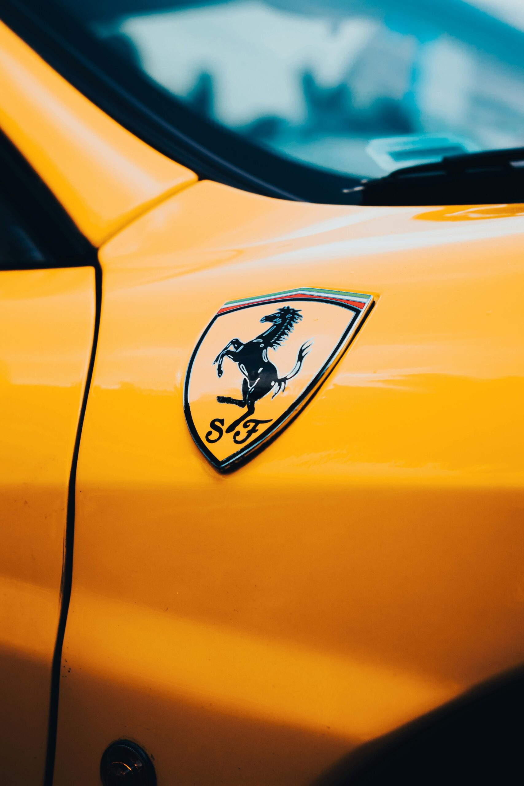 about-us Detailed close-up of a Ferrari logo on a vibrant yellow car's body.